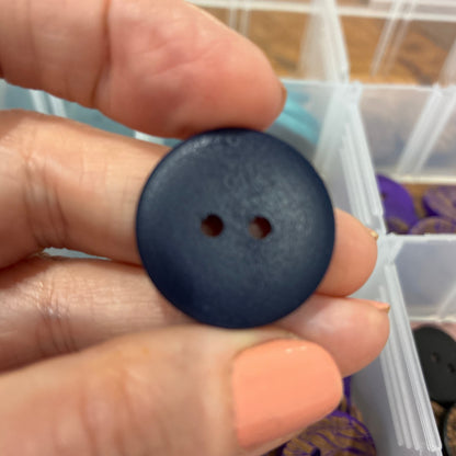 Hand holding a blue button with a clear container of buttons in the background
