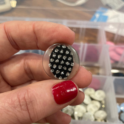 Hand holding a button with black and silver design against a background of colorful buttons.