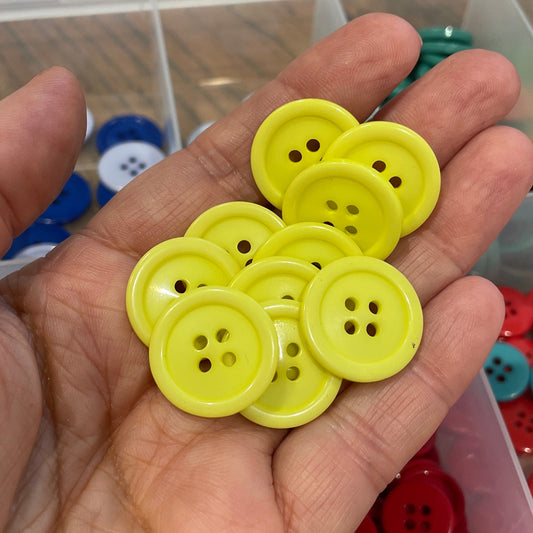 Hand holding yellow buttons with a container of colorful buttons in the background