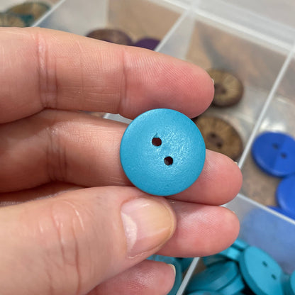 Hand holding a blue button with a container of buttons in the background