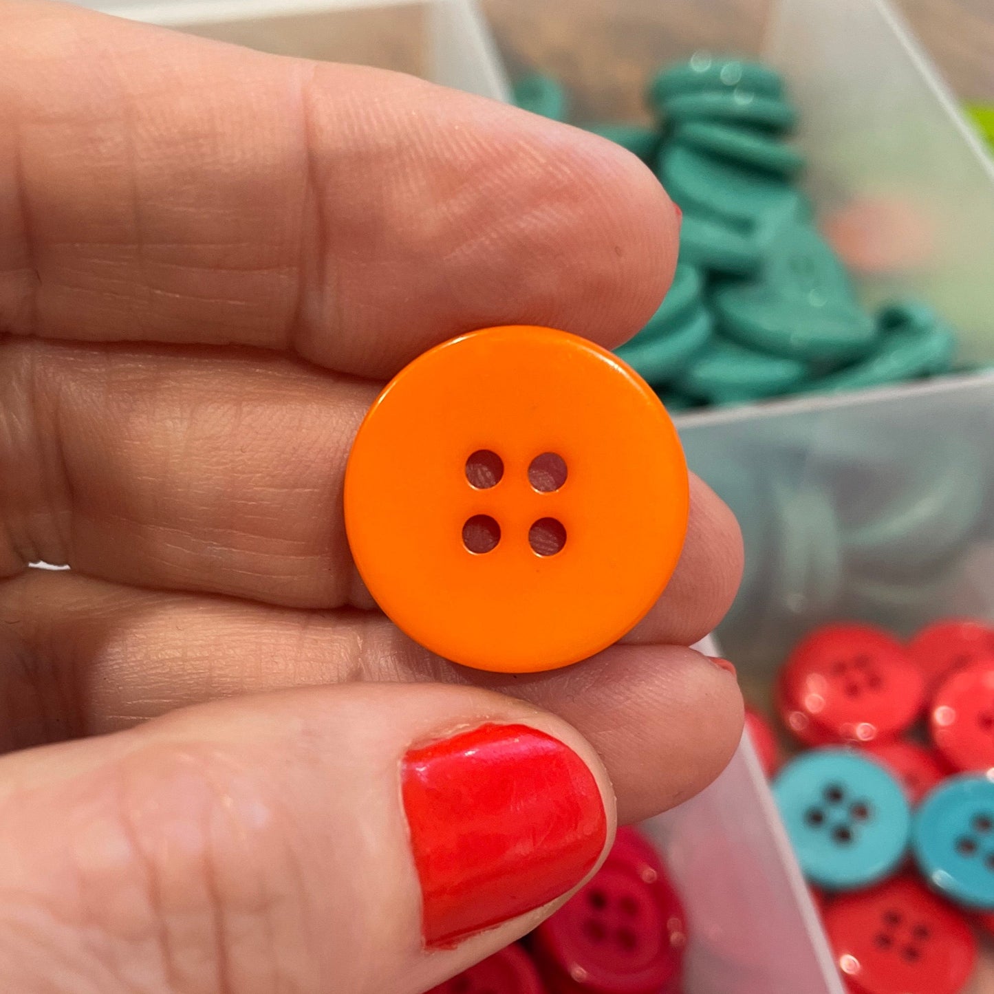 Hand holding an orange button with a container of red buttons in the background