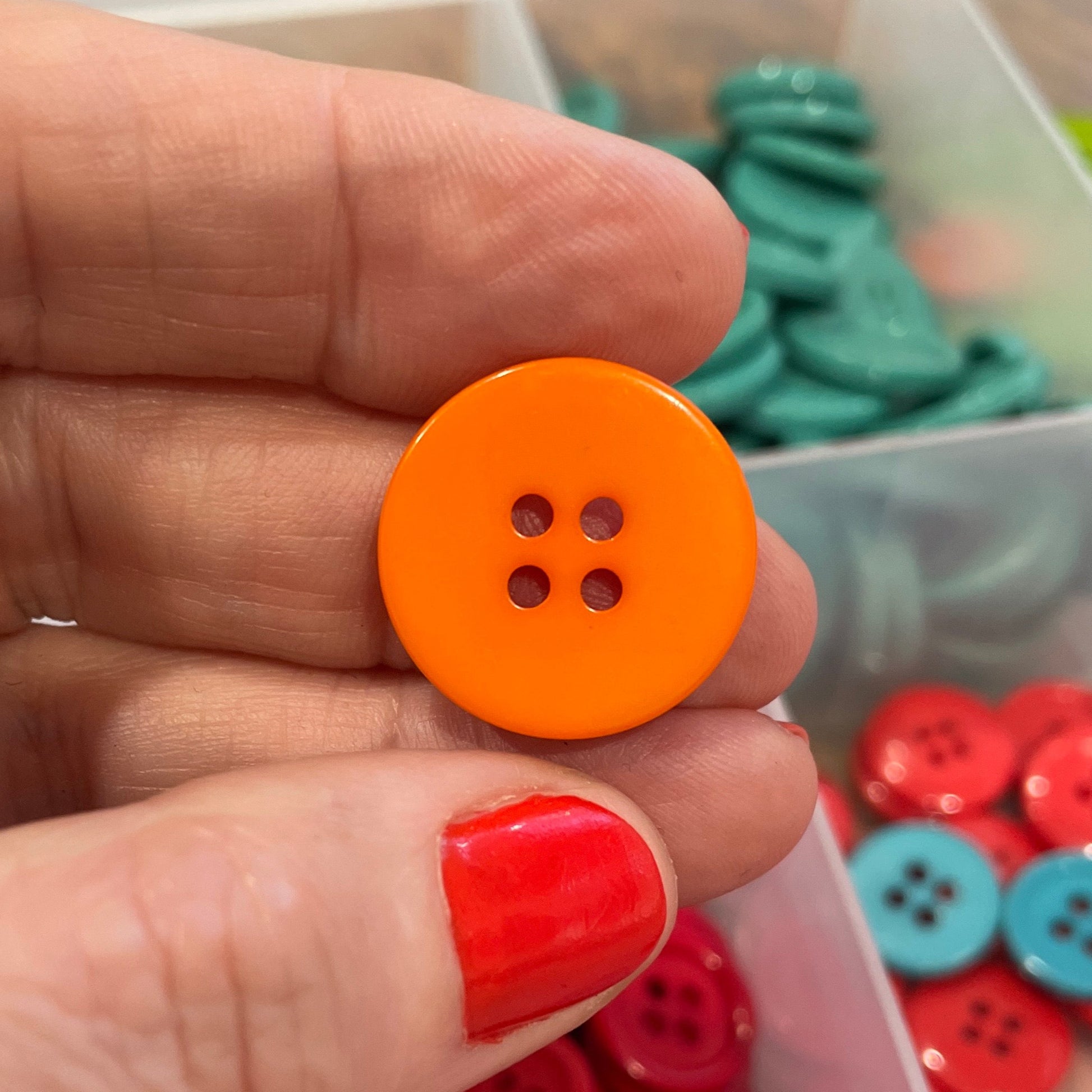Hand holding an orange button with a container of red buttons in the background