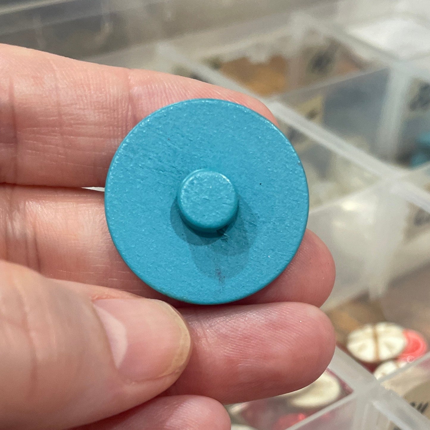 Hand holding a blue button with a clear container of buttons in the background