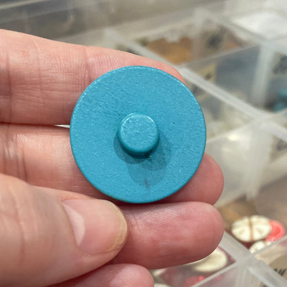 Hand holding a blue button with a clear container of buttons in the background