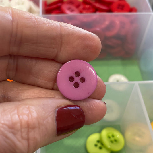 Hand holding a pink button with a container of assorted buttons in the background