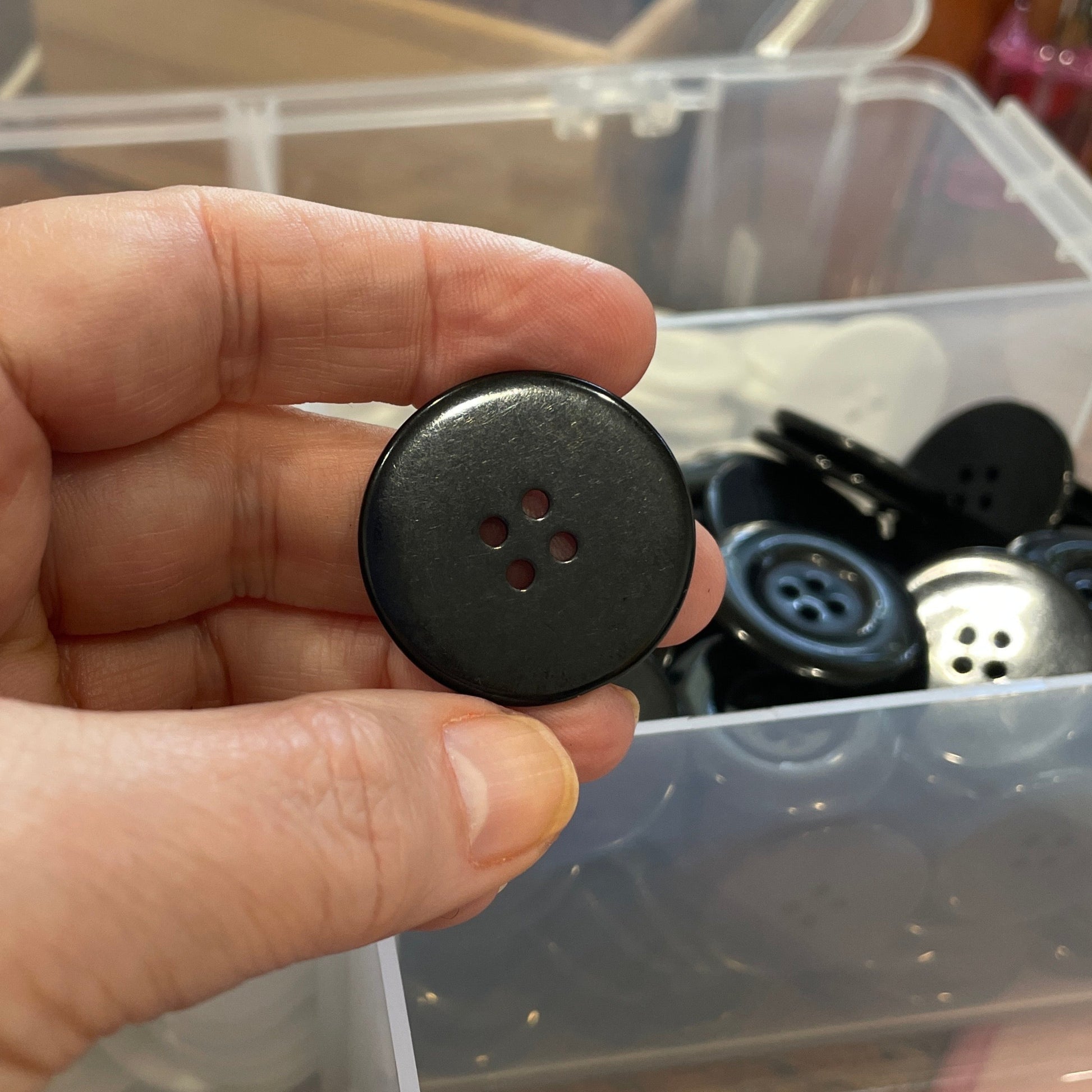 Hand holding a black button with a blurred background of a container with buttons.