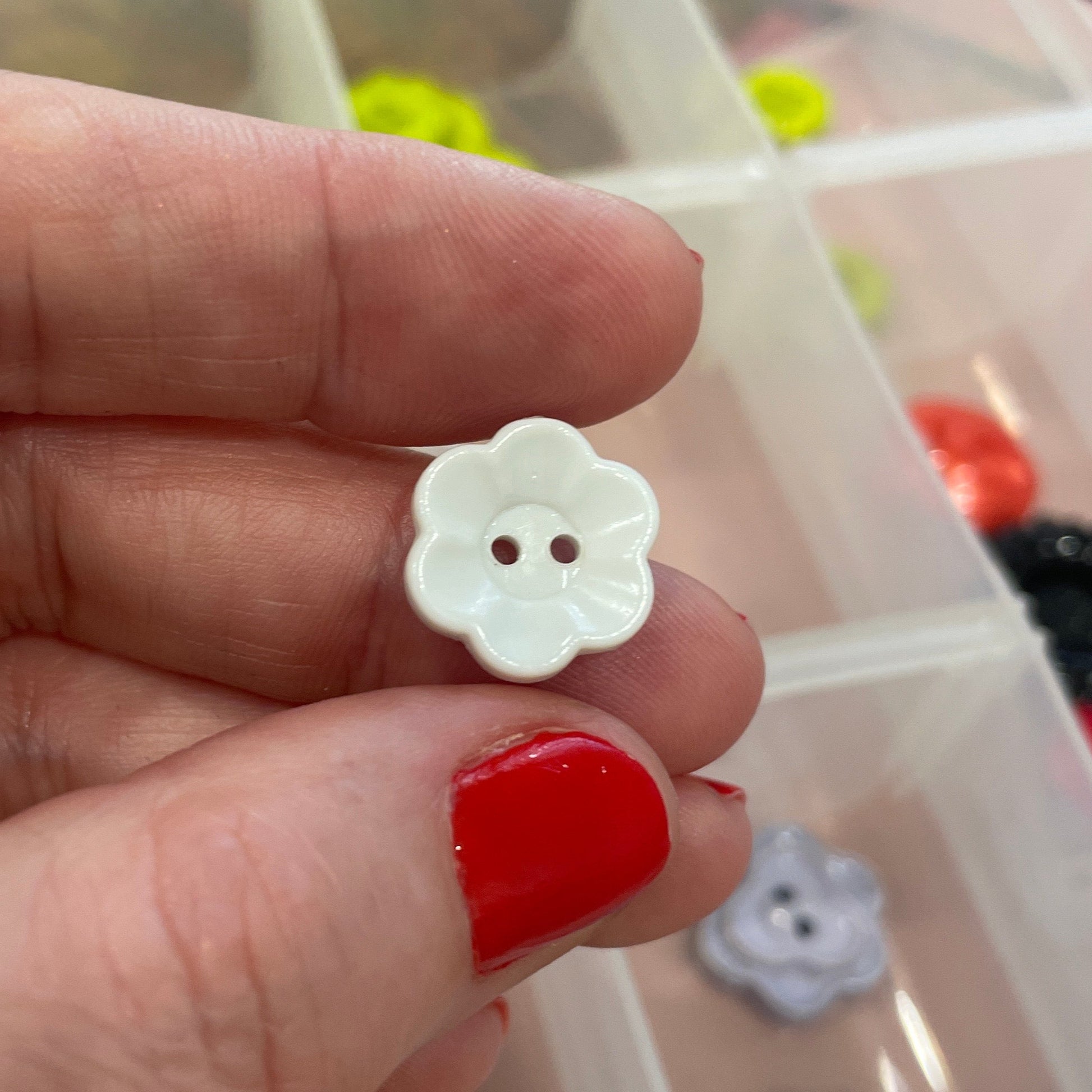 Hand holding a white flower-shaped button with a clear container of buttons in the background