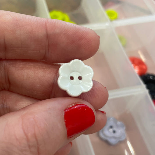 Hand holding a white flower-shaped button with a clear container of buttons in the background