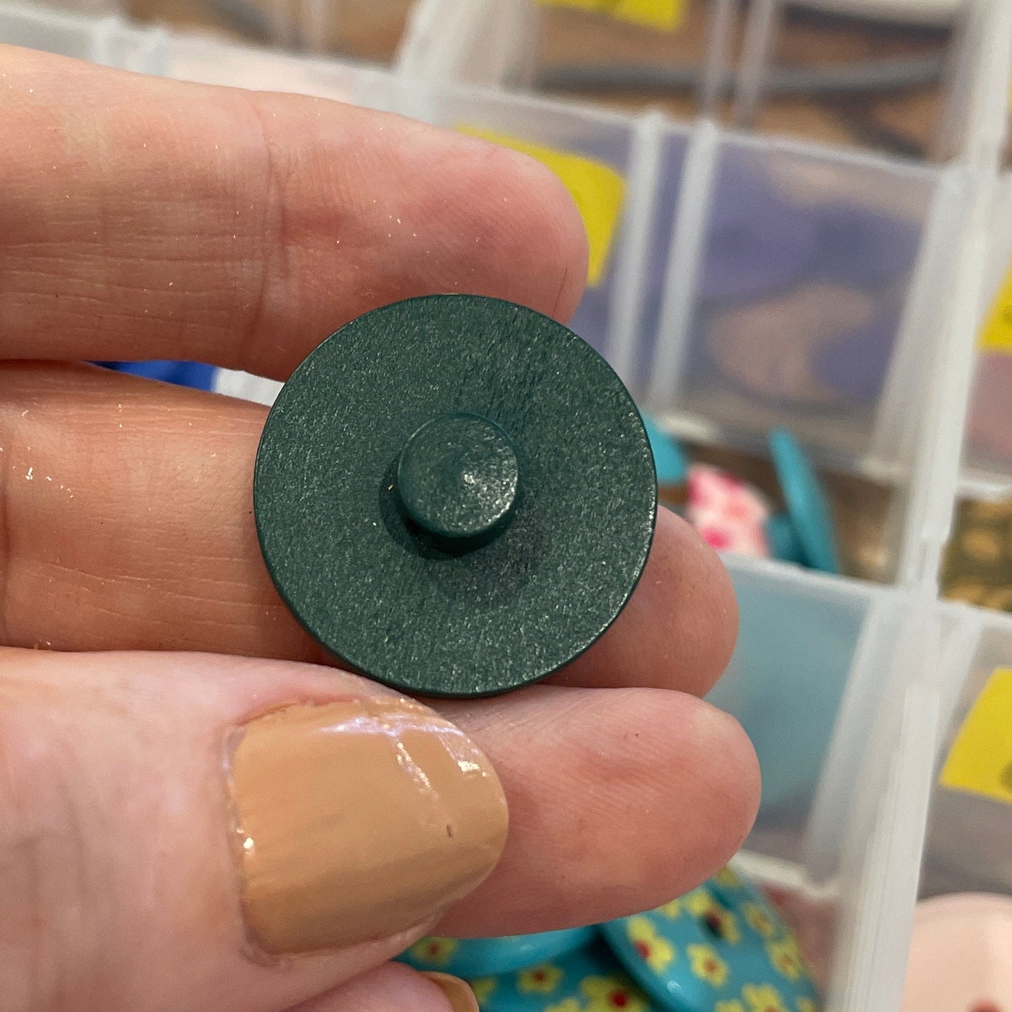 Hand holding a green button with a background of button containers.