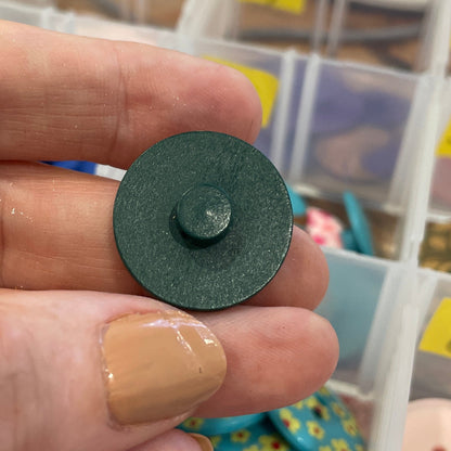 Hand holding a green button with a background of button containers.