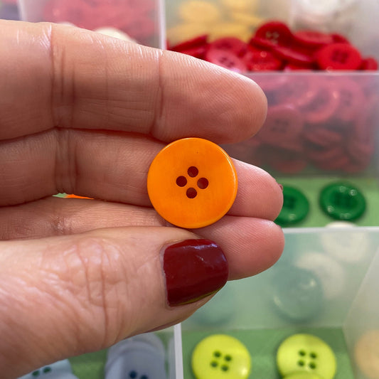 Hand holding an orange button with a transparent container of assorted buttons in the background
