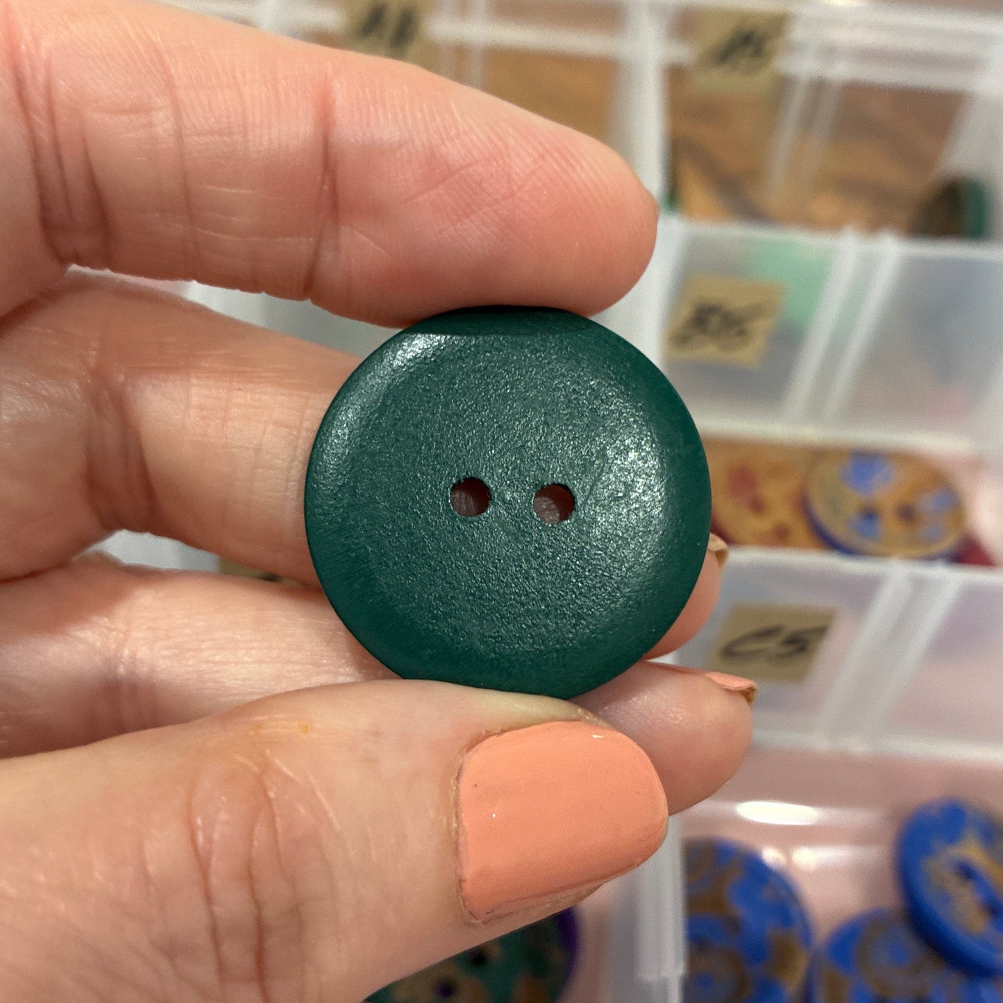 Hand holding a green button with a container of buttons in the background