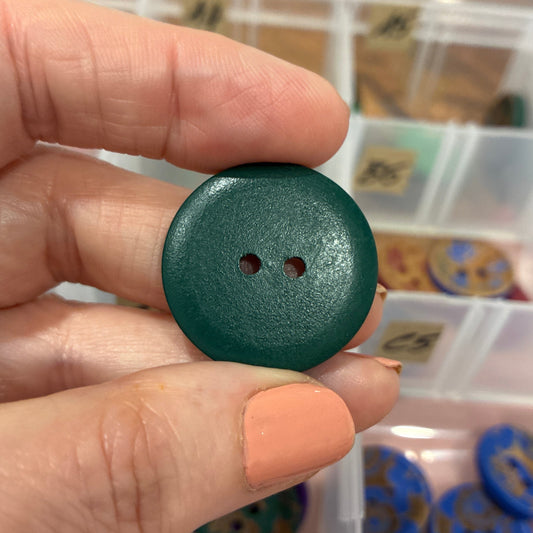 Hand holding a green button with a container of buttons in the background