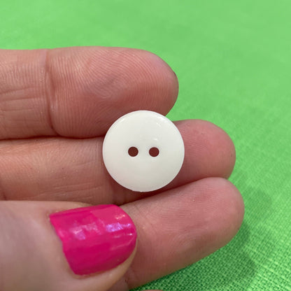 White button held between fingers against a green background