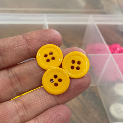 Yellow buttons held between fingers with a container of buttons in the background