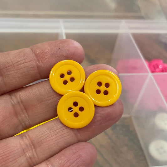 Yellow buttons held between fingers with a container of buttons in the background