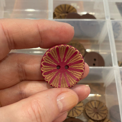 Hand holding a decorative button with a container of various buttons in the background