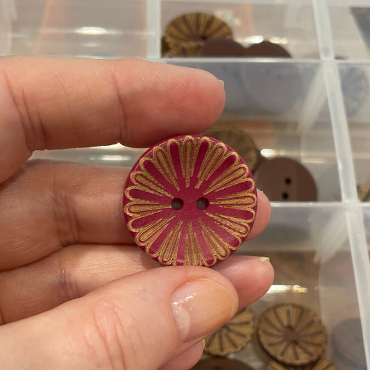 Hand holding a decorative button with a container of various buttons in the background