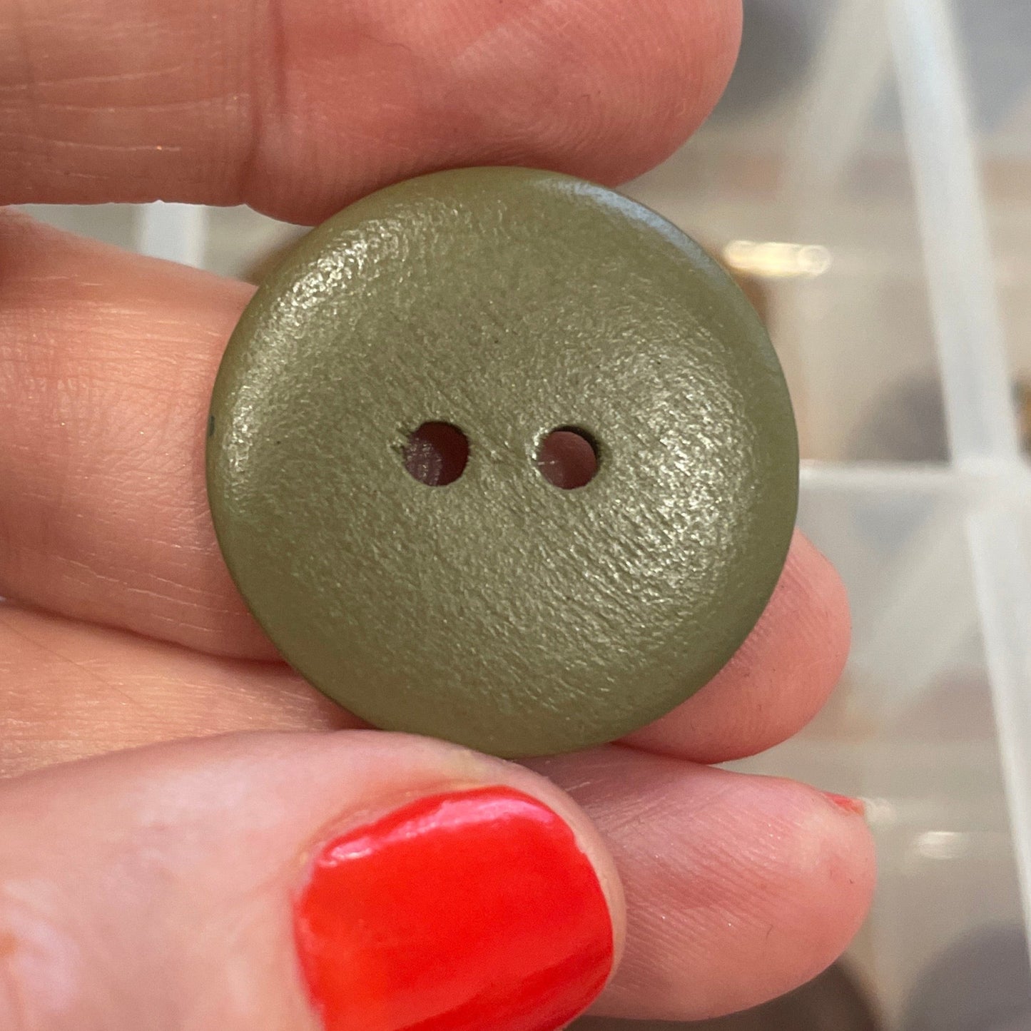 Hand holding a green button with a background of various buttons in a box.