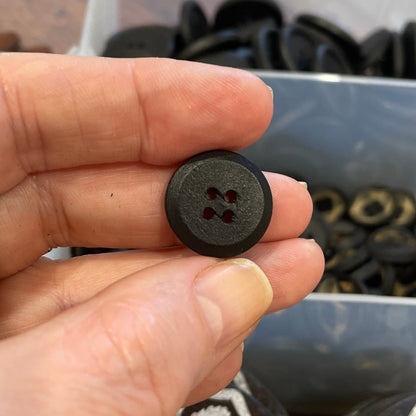 Person holding a black button with a blurred background of buttons and containers.