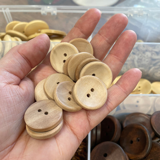Hand holding a collection of wooden buttons with a blurred background of more buttons.