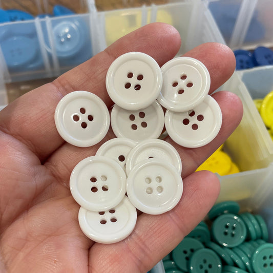 Hand holding white buttons with a container of colorful buttons in the background