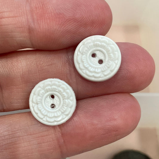 Two white buttons held between fingers with a blurred background of more buttons.