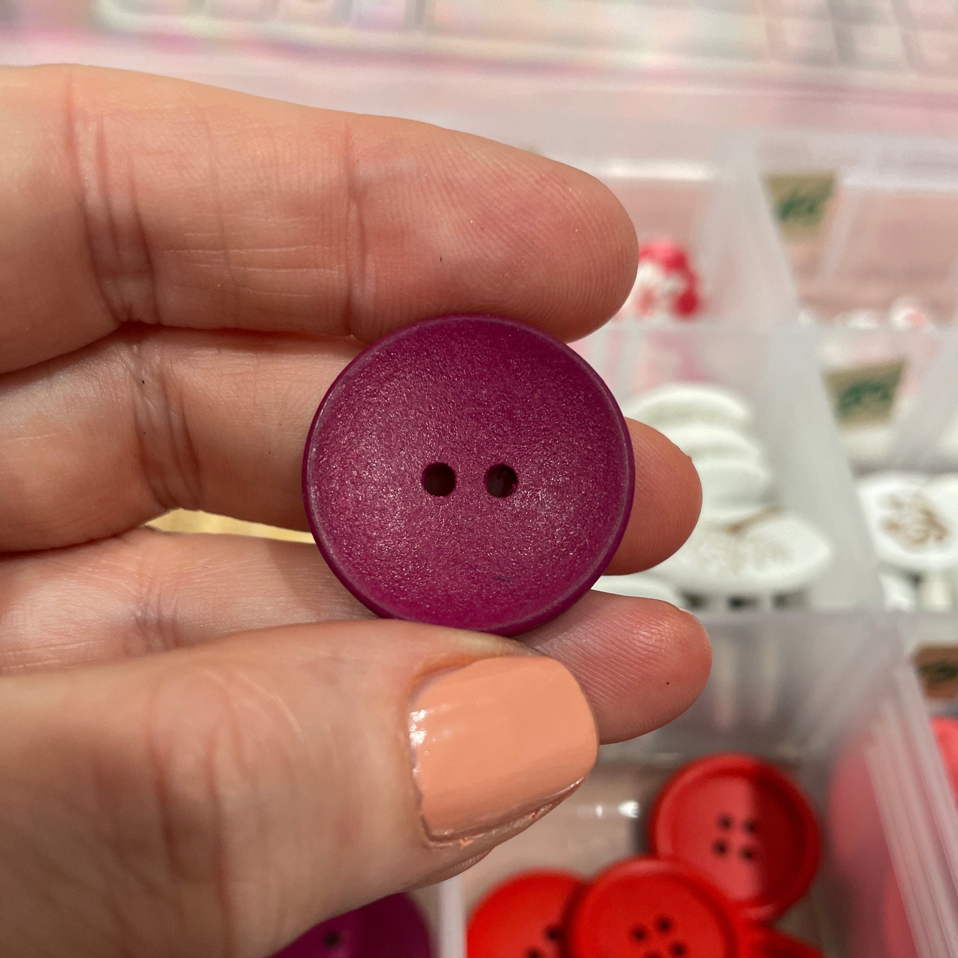 Purple button held between fingers with a container of buttons in the background