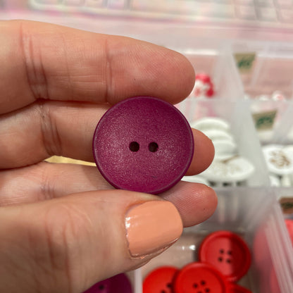 Purple button held between fingers with a container of buttons in the background