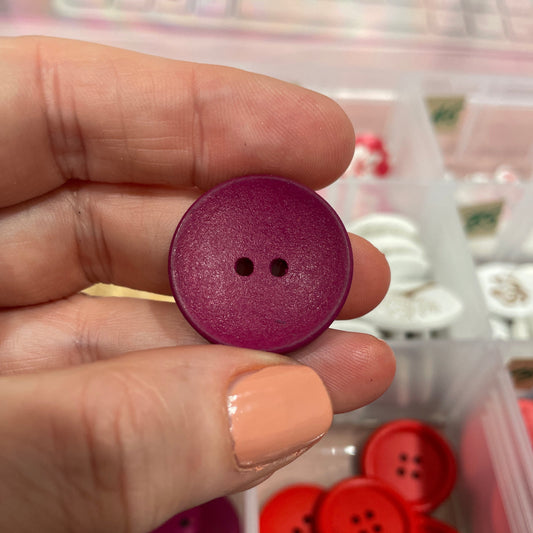 Purple button held between fingers with a container of buttons in the background