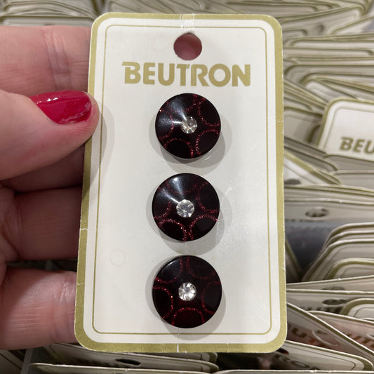 Beutron buttons on a display card held by a hand with red nail polish.