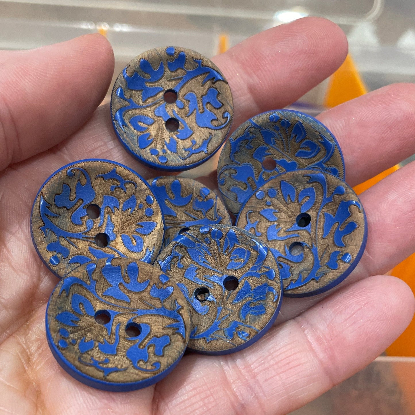 Hand holding blue decorative buttons with a blurred background of more buttons and containers.