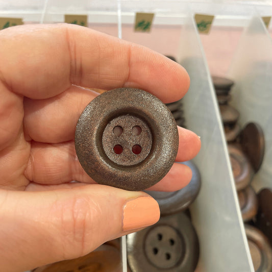Hand holding a metallic button with a blurred background of buttons on a rack.