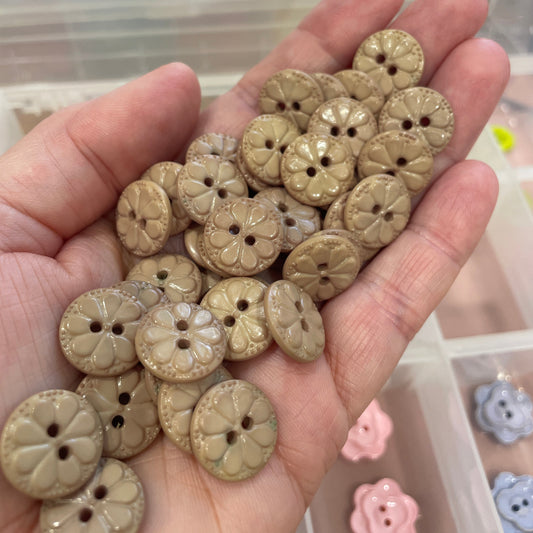 Hand holding a collection of beige buttons with floral designs.