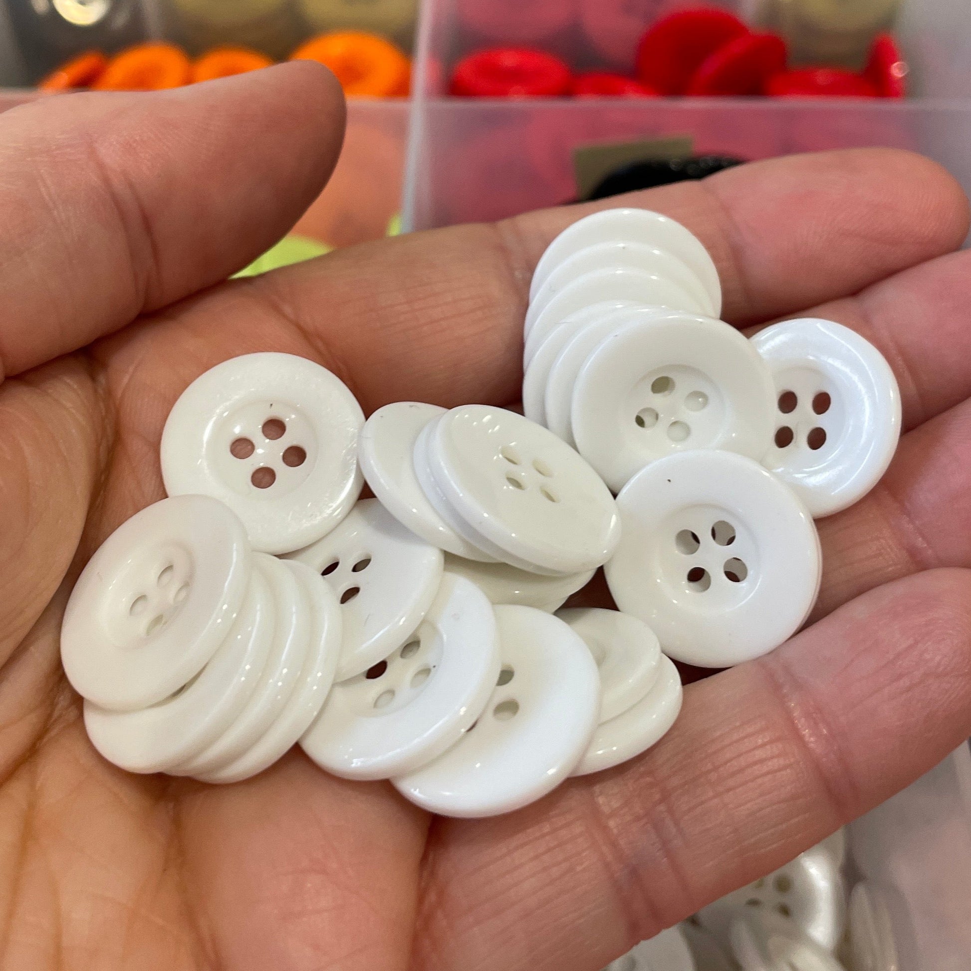 Hand holding white buttons with a button collection organizer in the background