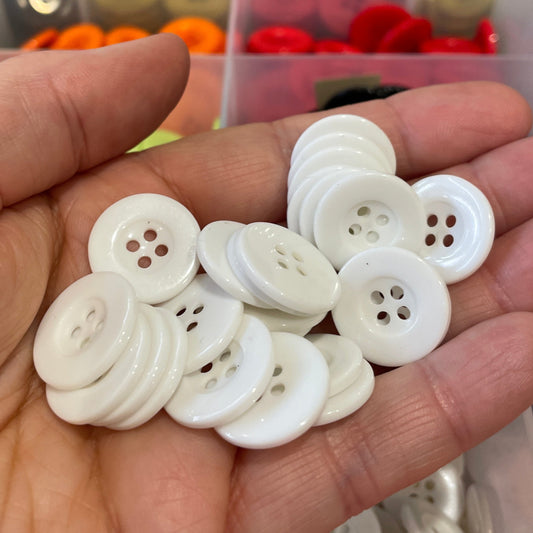 Hand holding white buttons with a button collection organizer in the background