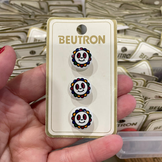 Hand holding a card with three earrings featuring smiley face designs, branded 'BEUTRON'.