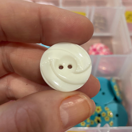 White button held between fingers with a container of buttons in the background