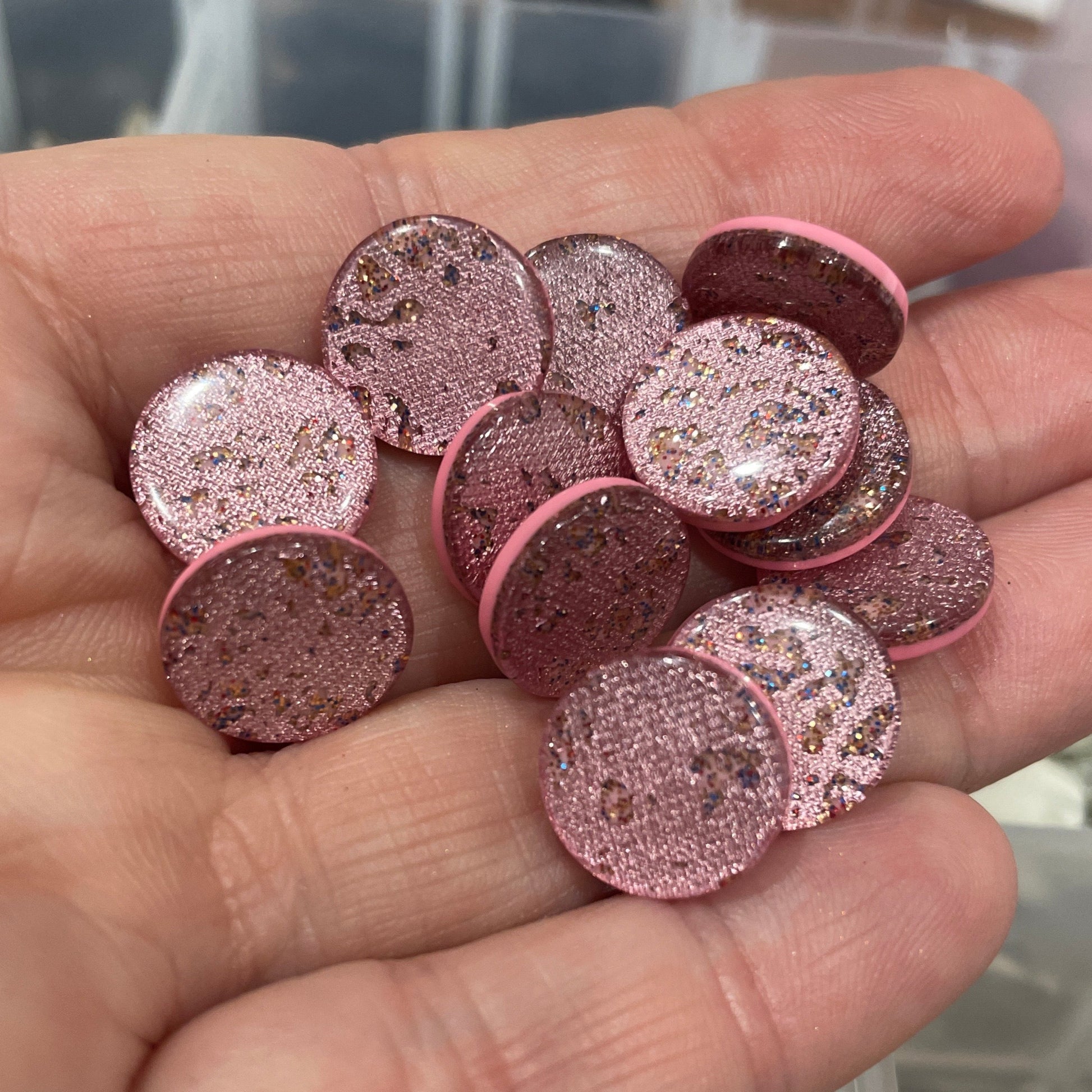 Hand holding pink glittery circular objects with a blurred background