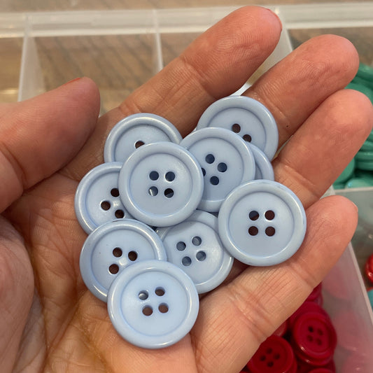 Hand holding gray buttons with a background of colorful buttons in a container.