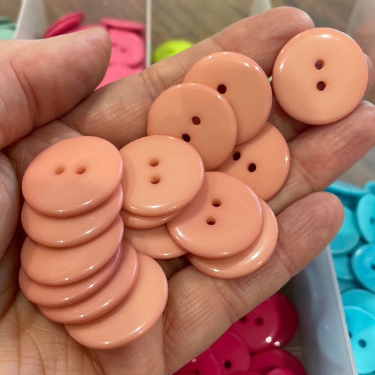 Hand holding peach-colored buttons with a background of colorful buttons in a container.