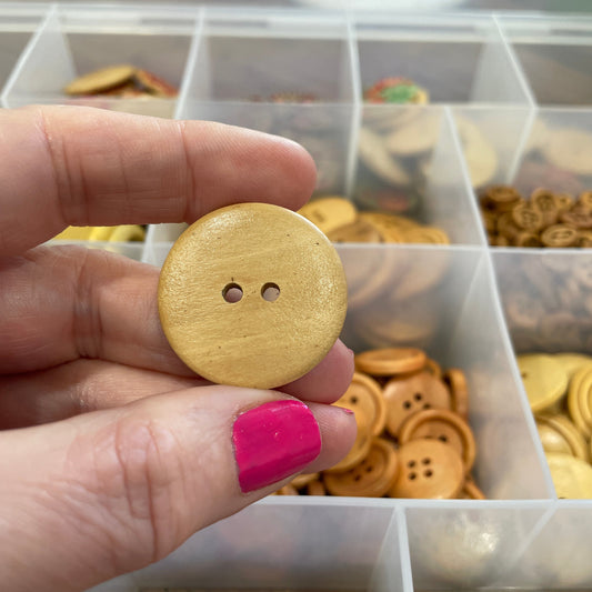 Hand holding a gold button in front of a container of various buttons