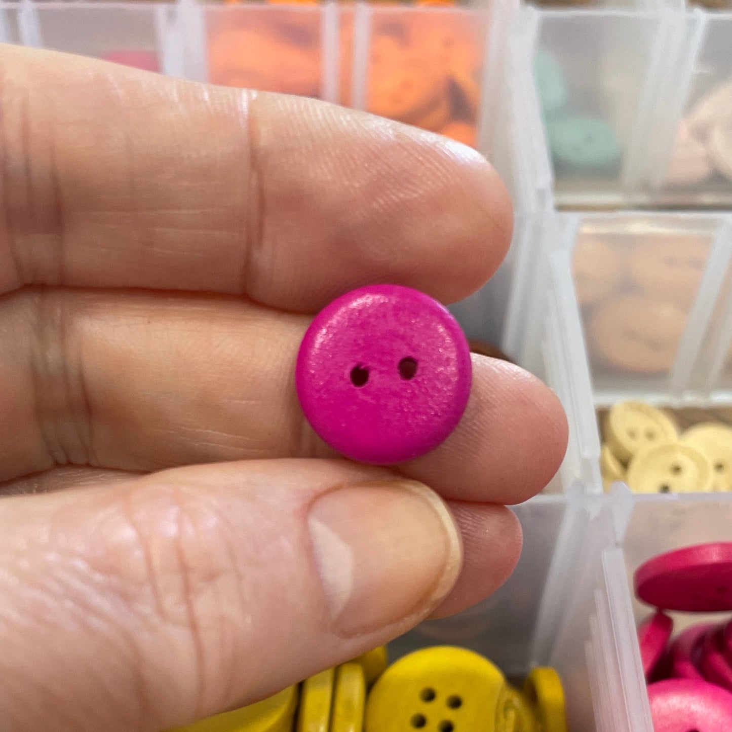 Hand holding a pink button with a container of colorful buttons in the background