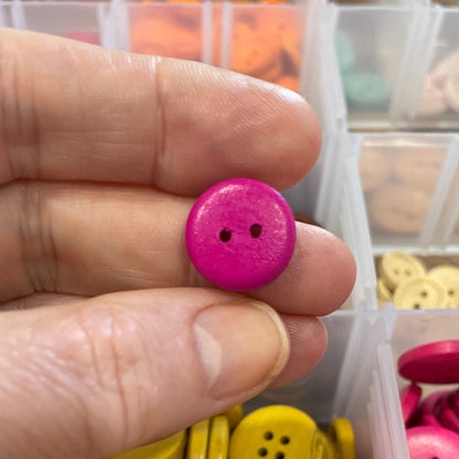 Hand holding a pink button with a container of colorful buttons in the background