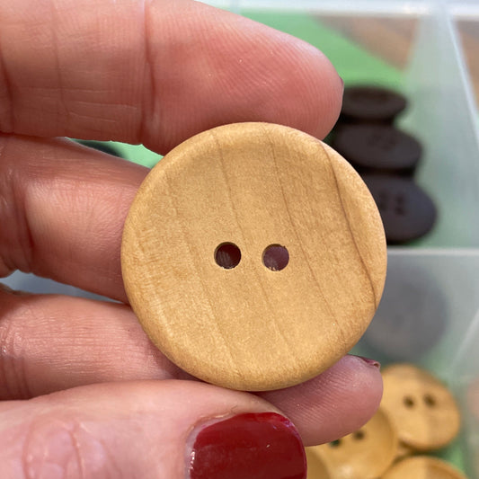 Wooden button held by a hand with a background of button assortment