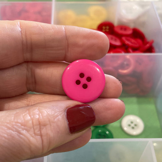 Hand holding a pink button with a background of colorful buttons in a container