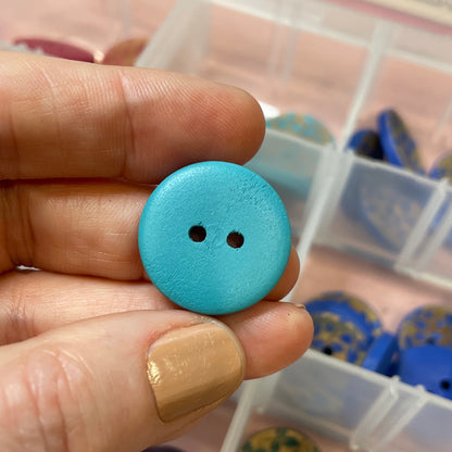 Hand holding a blue button with a container of buttons in the background
