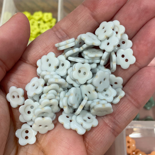 Hand holding small white floral beads with a blurred background of a storage box.