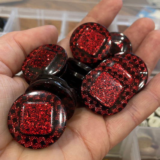 Hand holding red glittery buttons with a blurred background of a container with more buttons.