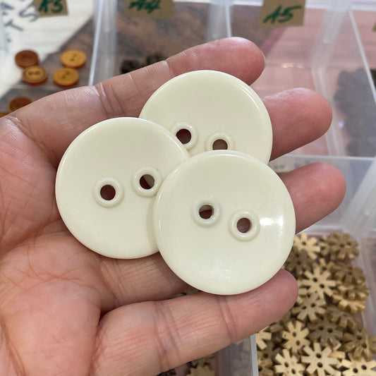 Hand holding a white button with a container of decorative items in the background